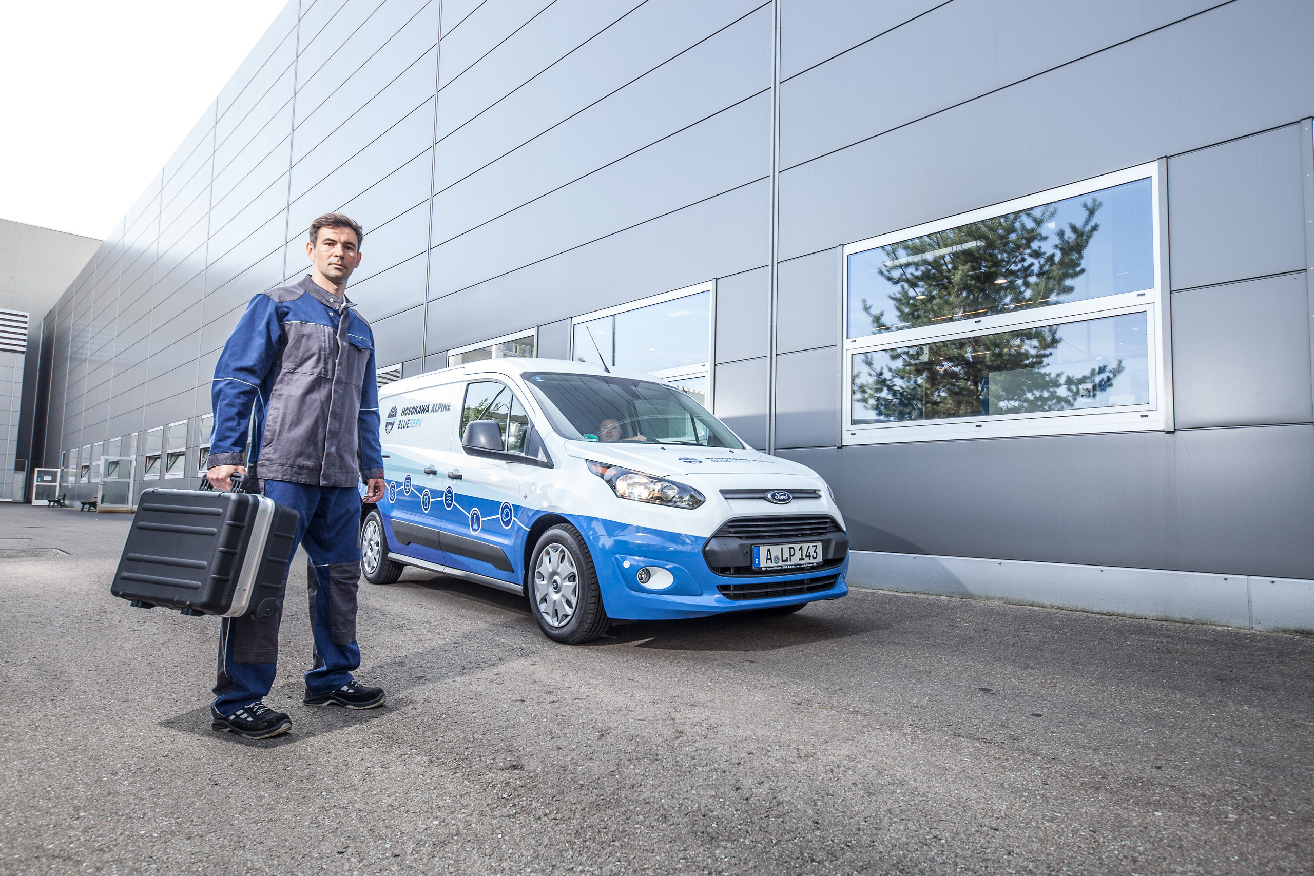 Empleado de Blueserv con una caja de herramientas delante de un coche Blueserv de marca